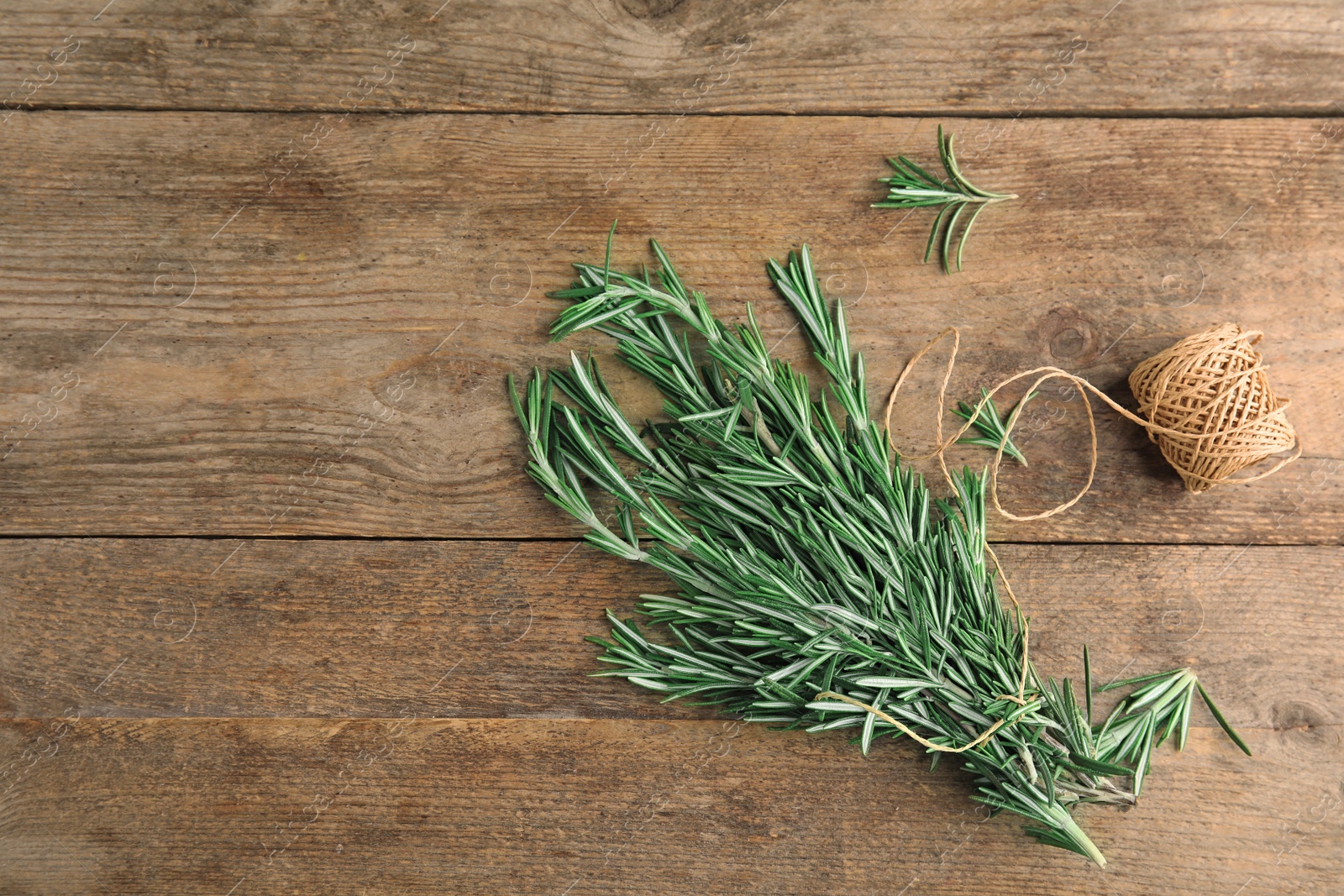 Photo of Fresh rosemary branches and twine on wooden table, flat lay. Space for text