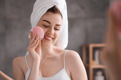 Photo of Washing face. Young woman with cleansing brush near mirror in bathroom