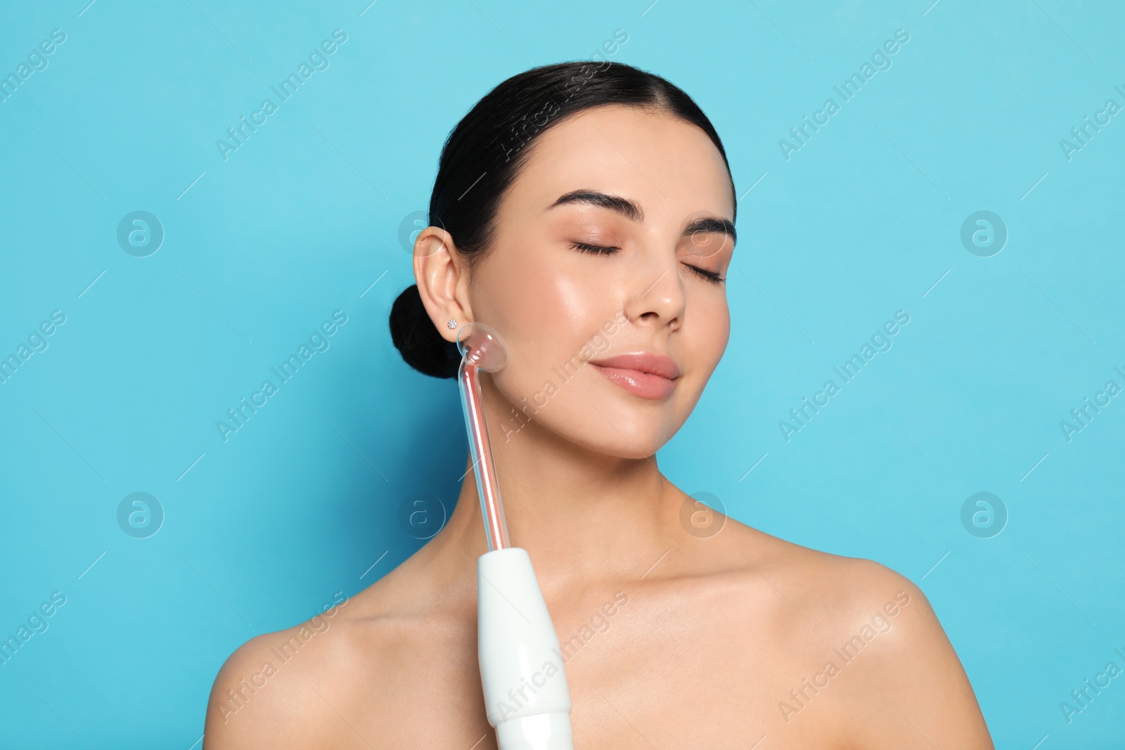 Photo of Woman using high frequency darsonval device on light blue background