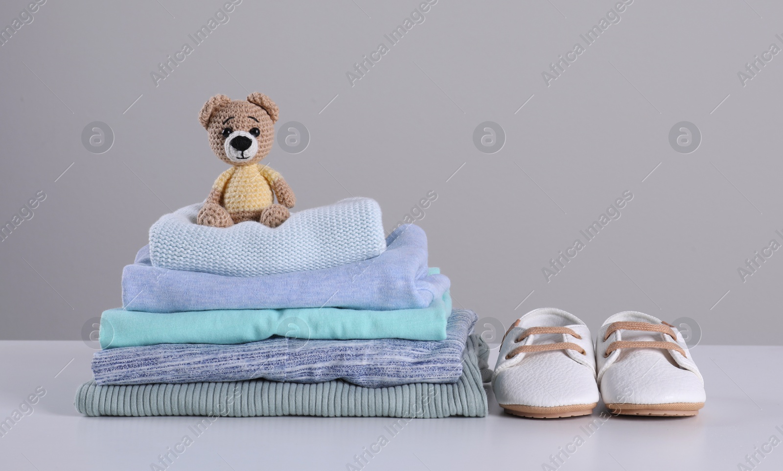 Photo of Stack of clean baby's clothes, toy and small shoes on table against light grey background. Space for text