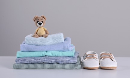 Photo of Stack of clean baby's clothes, toy and small shoes on table against light grey background. Space for text