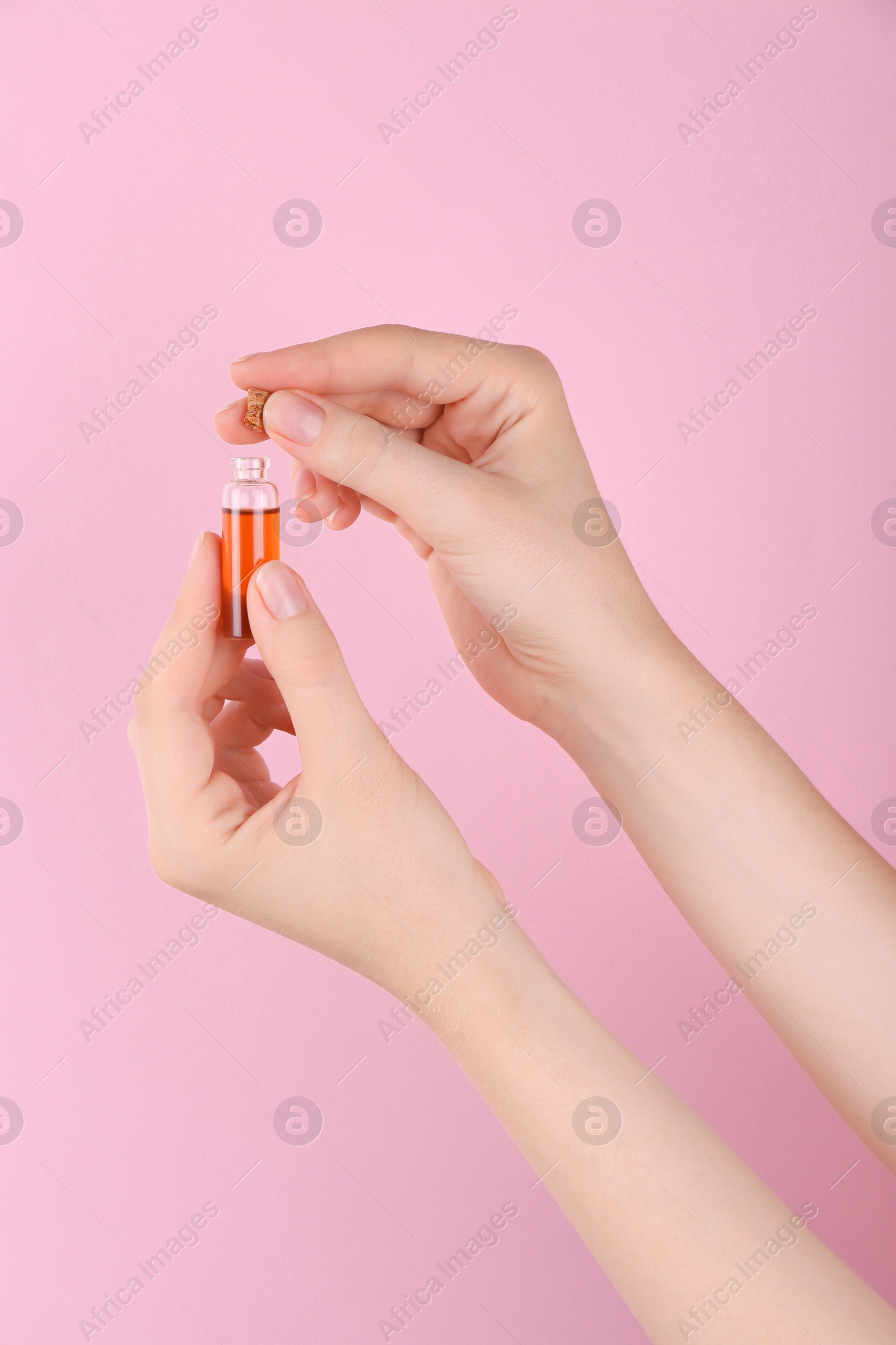 Photo of Woman holding bottle of essential oil on pink background, closeup