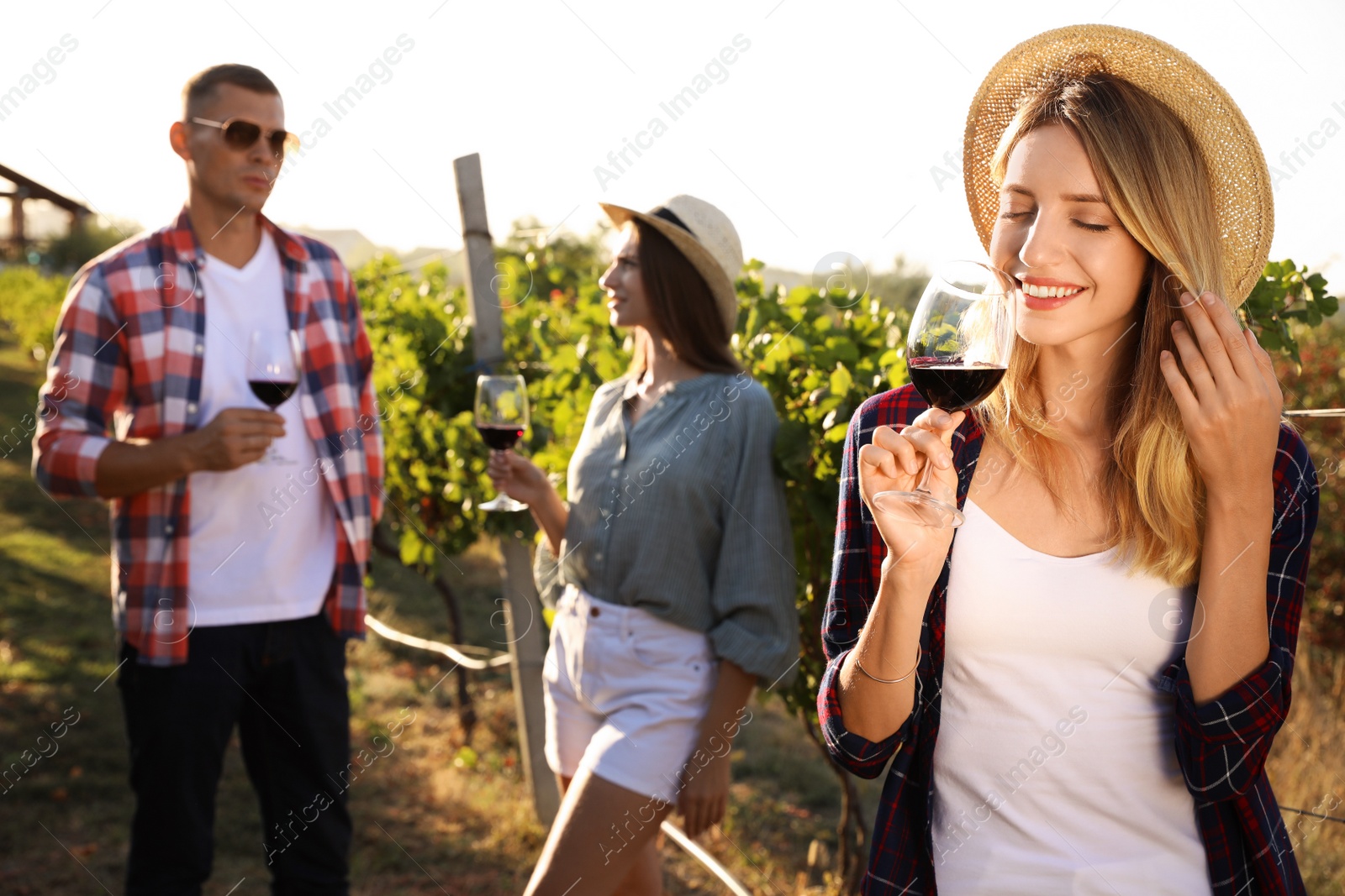 Photo of Beautiful young woman with glass of wine and her friends in vineyard on sunny day