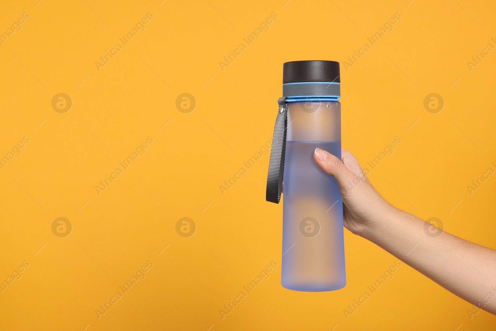 Photo of Woman holding bottle of water on orange background, closeup. Space for text