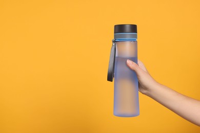 Woman holding bottle of water on orange background, closeup. Space for text