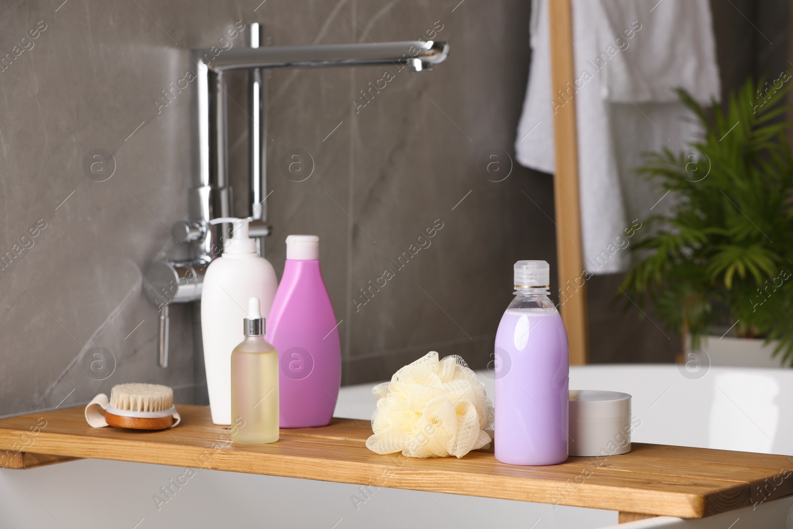 Photo of Wooden bath tray with shampoo, hair oil and other toiletries on tub indoors