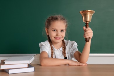 Photo of Pupil with school bell sitting at desk near chalkboard in classroom