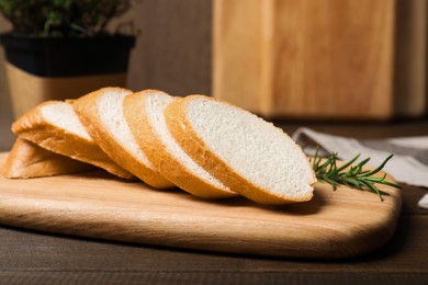 Photo of Cut tasty baguette with rosemary on wooden table