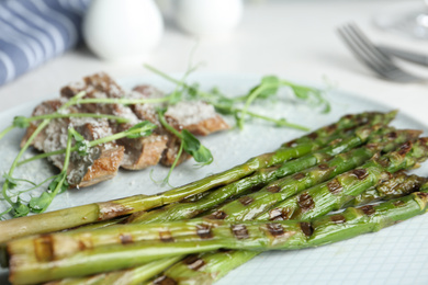 Photo of Tasty meat served with grilled asparagus on plate, closeup
