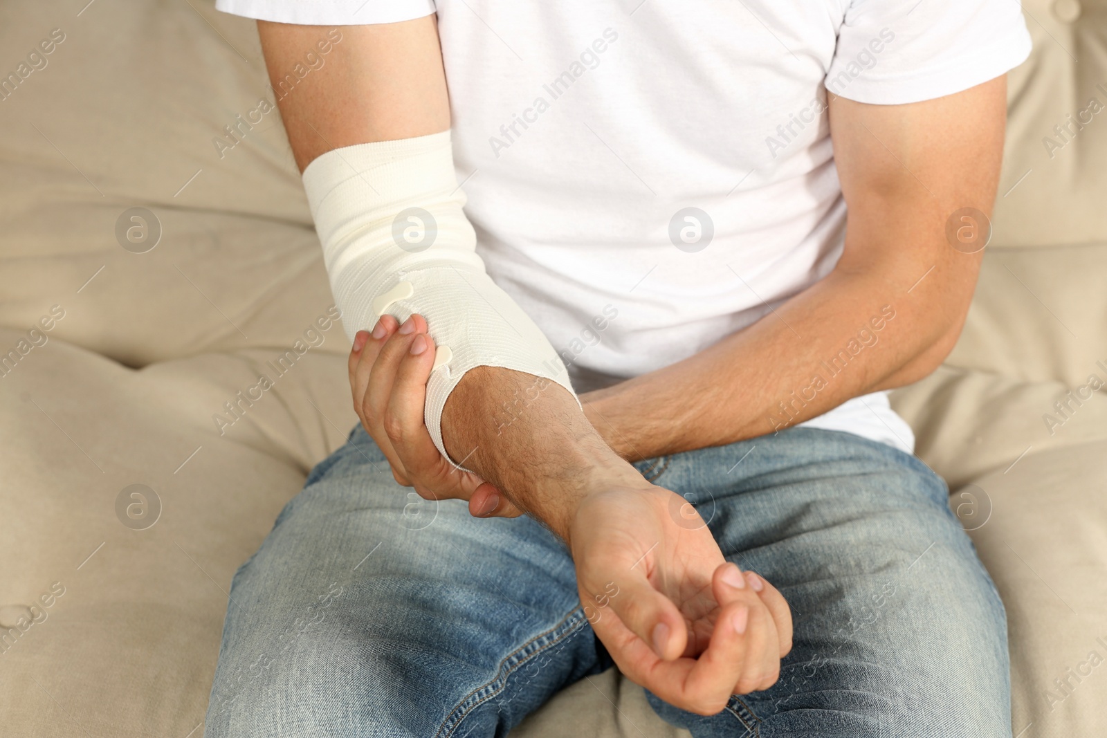 Photo of Man with arm wrapped in medical bandage on sofa, closeup