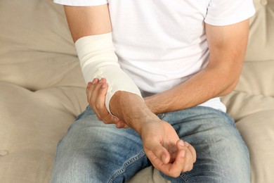 Photo of Man with arm wrapped in medical bandage on sofa, closeup