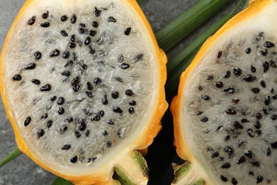Photo of Delicious cut dragon fruit (pitahaya) and green tropical leaf on grey table, closeup