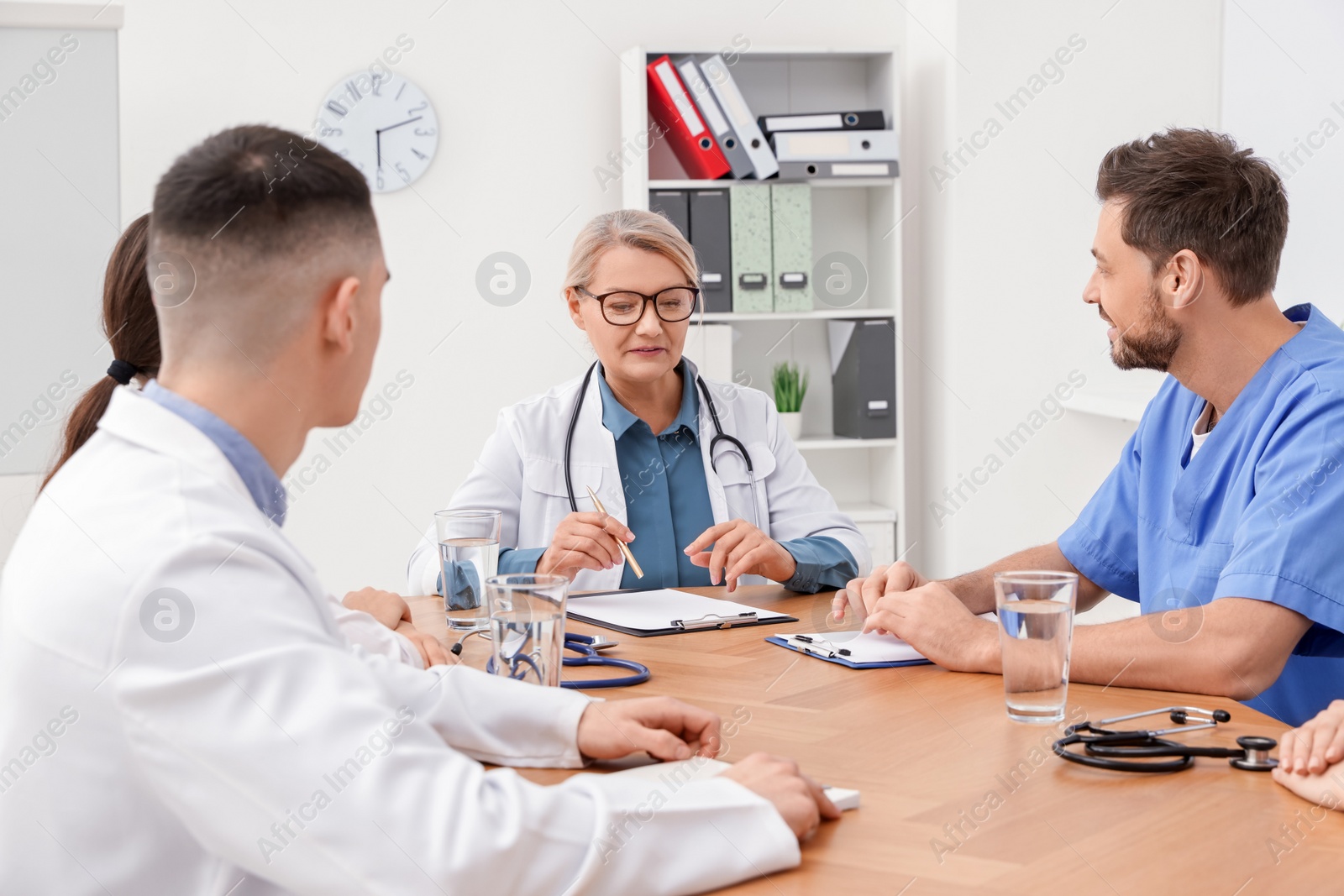 Photo of Medical conference. Team of doctors having discussion with speaker at wooden table in clinic