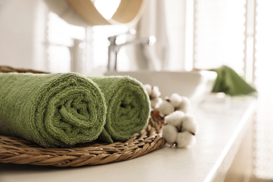 Photo of Wicker tray with clean towels and cotton flowers on countertop in bathroom. Space for text