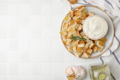Delicious crispy croutons with rosemary and sauce on white tiled table, flat lay. Space for text