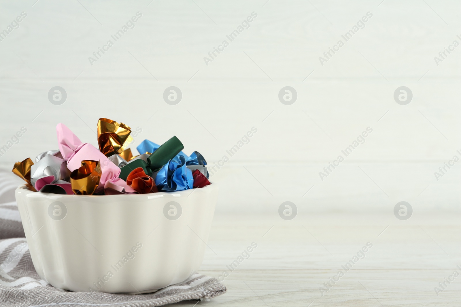 Photo of Candies in colorful wrappers on white wooden table, space for text