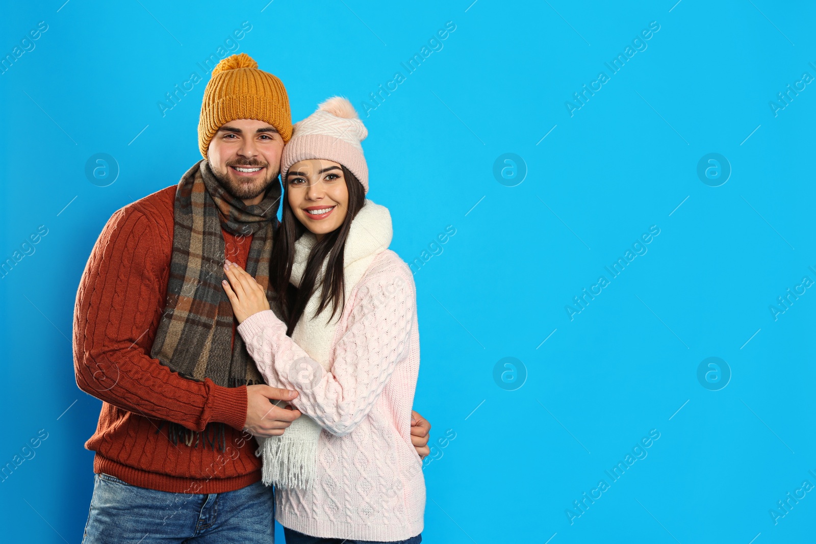 Photo of Happy young couple in warm clothes on blue background, space for text. Winter vacation