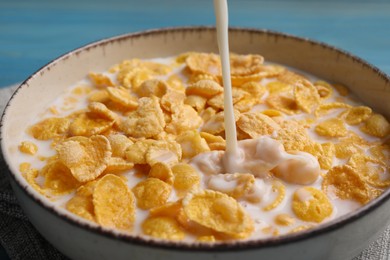 Photo of Pouring milk into bowl of tasty corn flakes at light blue table, closeup