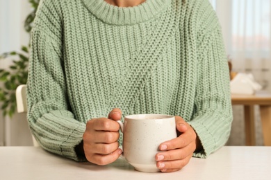 Woman holding cup of delicious cocoa drink at white table, closeup