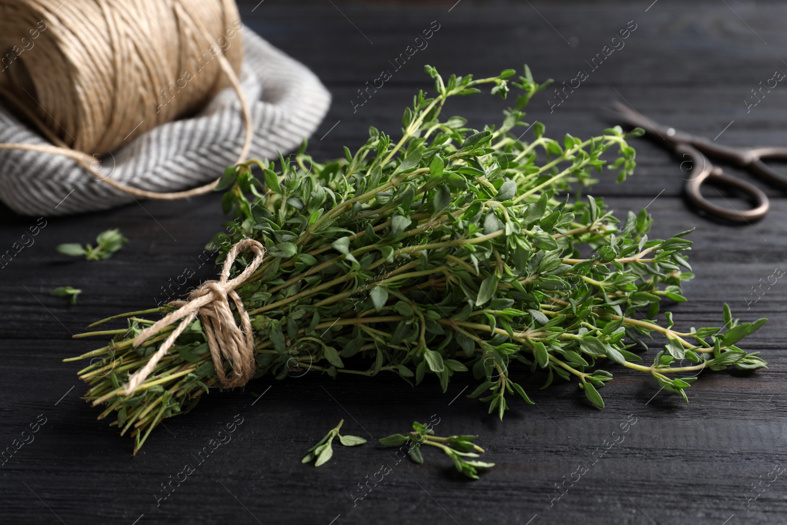 Photo of Bunch of aromatic thyme, scissors and twine on wooden table, closeup
