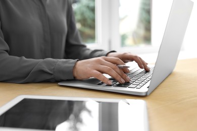 Woman with tablet and pen working on laptop at wooden table, closeup. Electronic document management