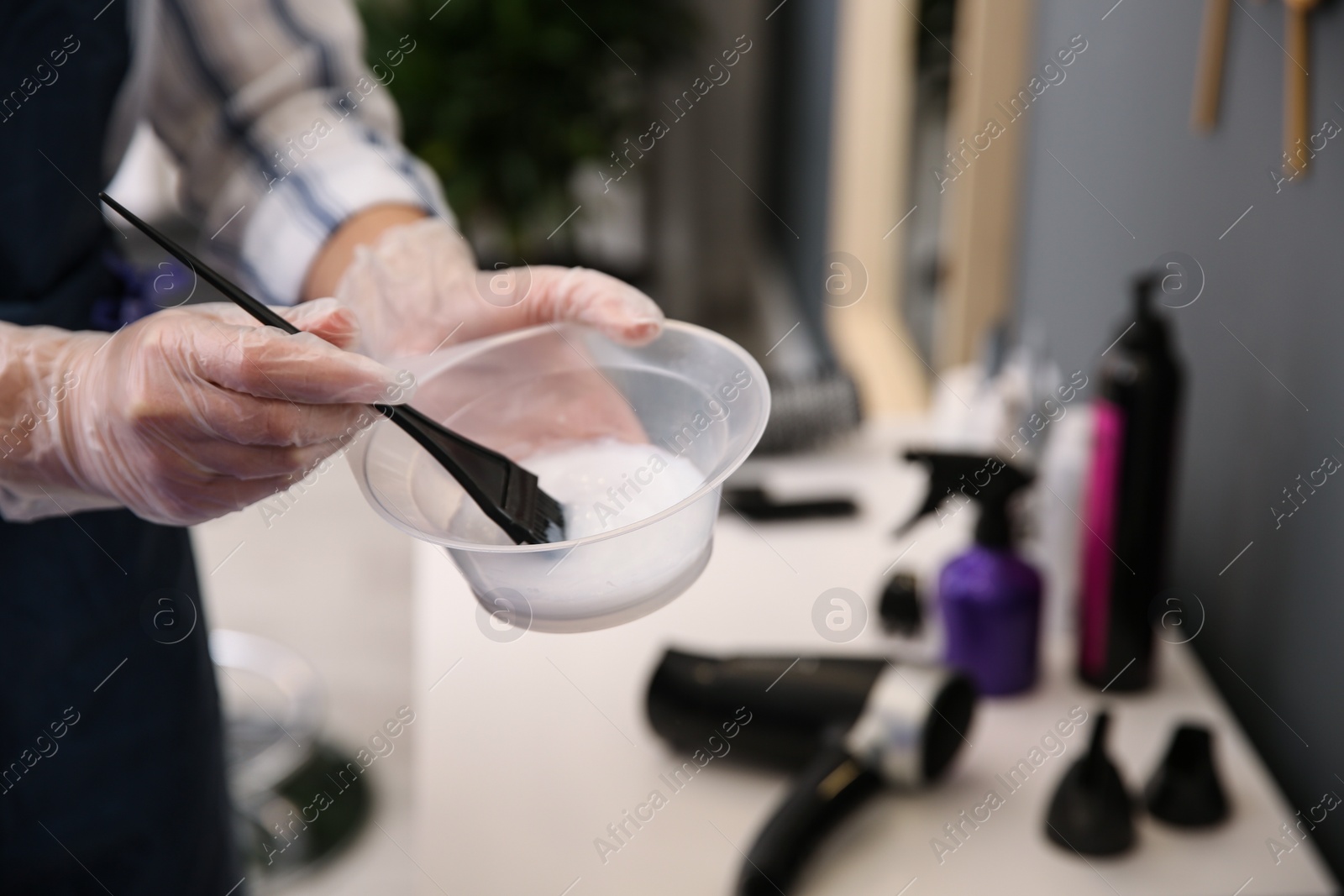 Photo of Professional hairdresser holding bowl with hair dye in beauty salon, closeup