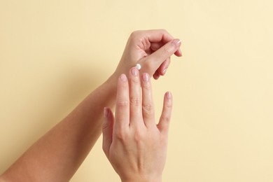 Photo of Woman applying cosmetic cream onto hand on beige background, closeup