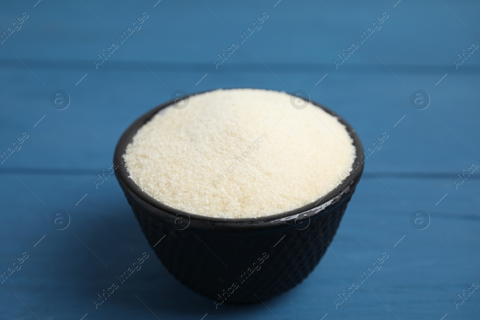 Photo of Gelatin powder in bowl on blue wooden table, closeup