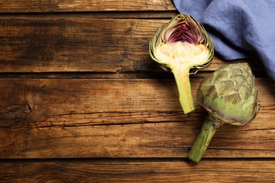 Photo of Cut and whole fresh raw artichokes on wooden table, flat lay. Space for text