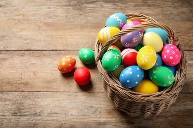 Photo of Colorful Easter eggs in basket on wooden background. Space for text