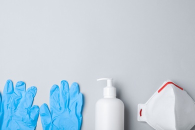 Medical gloves, respiratory mask and hand sanitizer on grey background, flat lay. Space for text