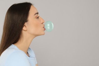 Beautiful woman blowing bubble gum on grey background. Space for text