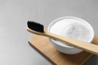 Bamboo toothbrush and bowl of baking soda on grey table, closeup. Space for text