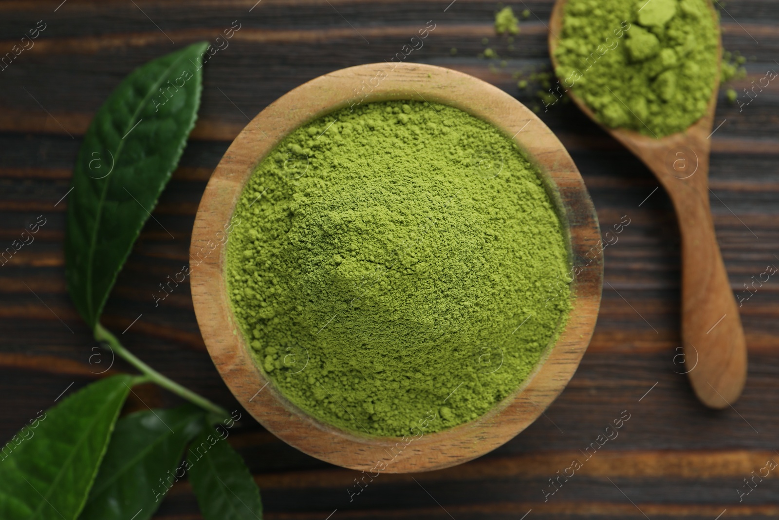 Photo of Bowl and spoon with green matcha powder on wooden table, flat lay