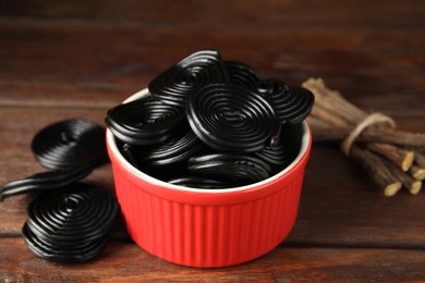 Photo of Tasty black candies and dried sticks of liquorice root on wooden table, closeup
