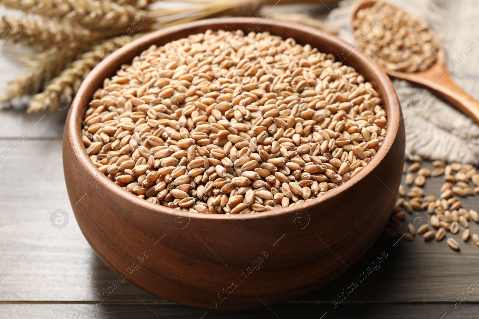 Photo of Wheat grains in bowl on wooden table, closeup