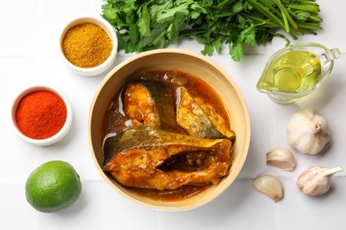 Photo of Tasty fish curry and ingredients on white tiled table, flat lay. Indian cuisine