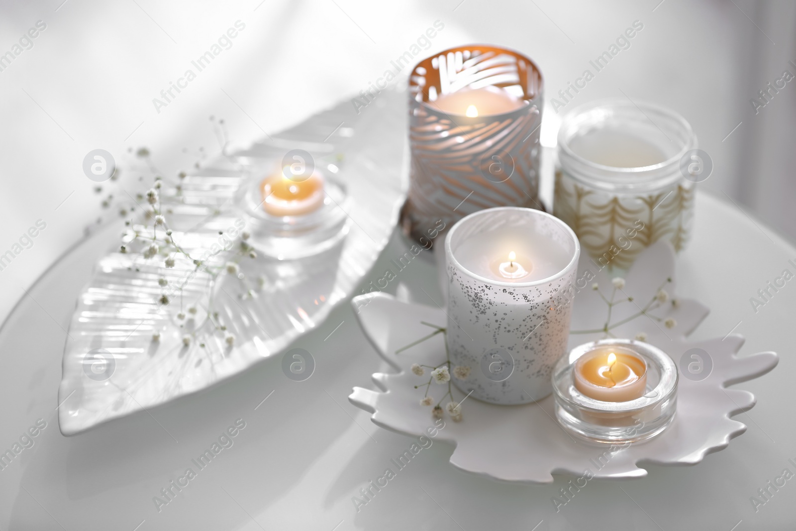 Photo of Burning candles in beautiful holders and flowers on table indoors