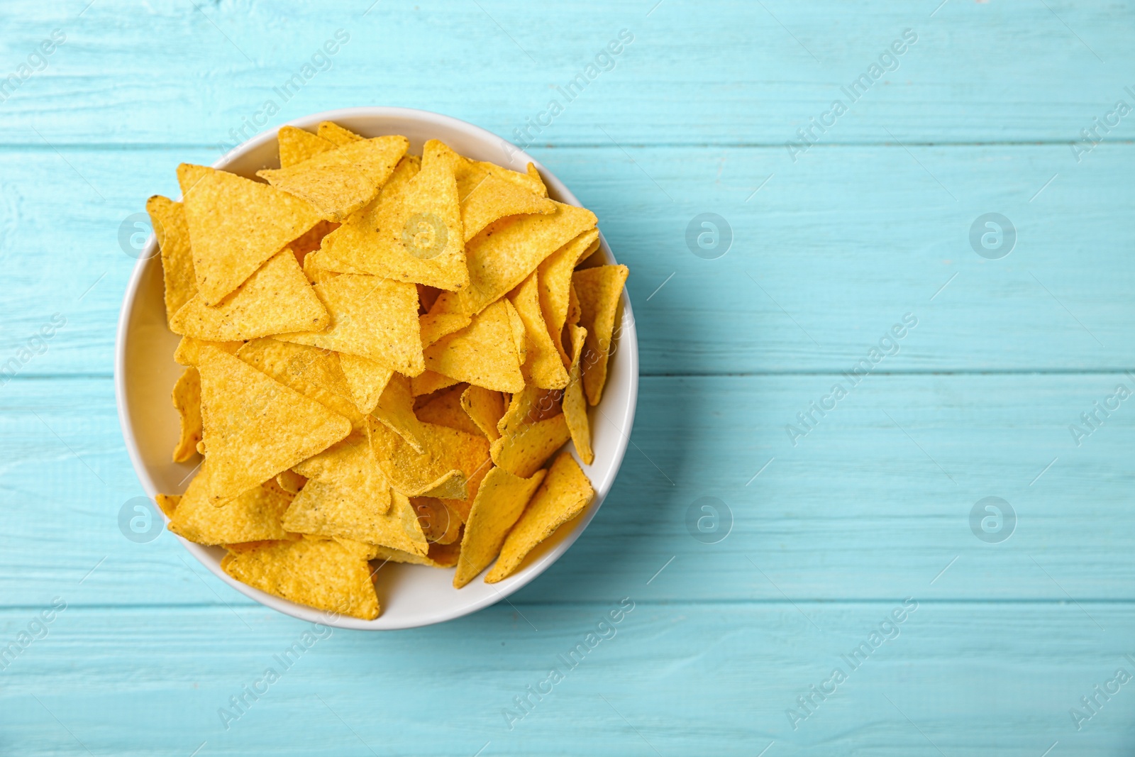Photo of Tasty mexican nachos chips in bowl on blue wooden table, top view. Space for text