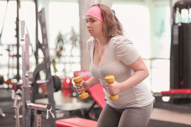 Photo of Overweight woman training with dumbbells in gym