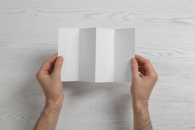 Man with blank brochure on wooden background, above view. Mock up for design