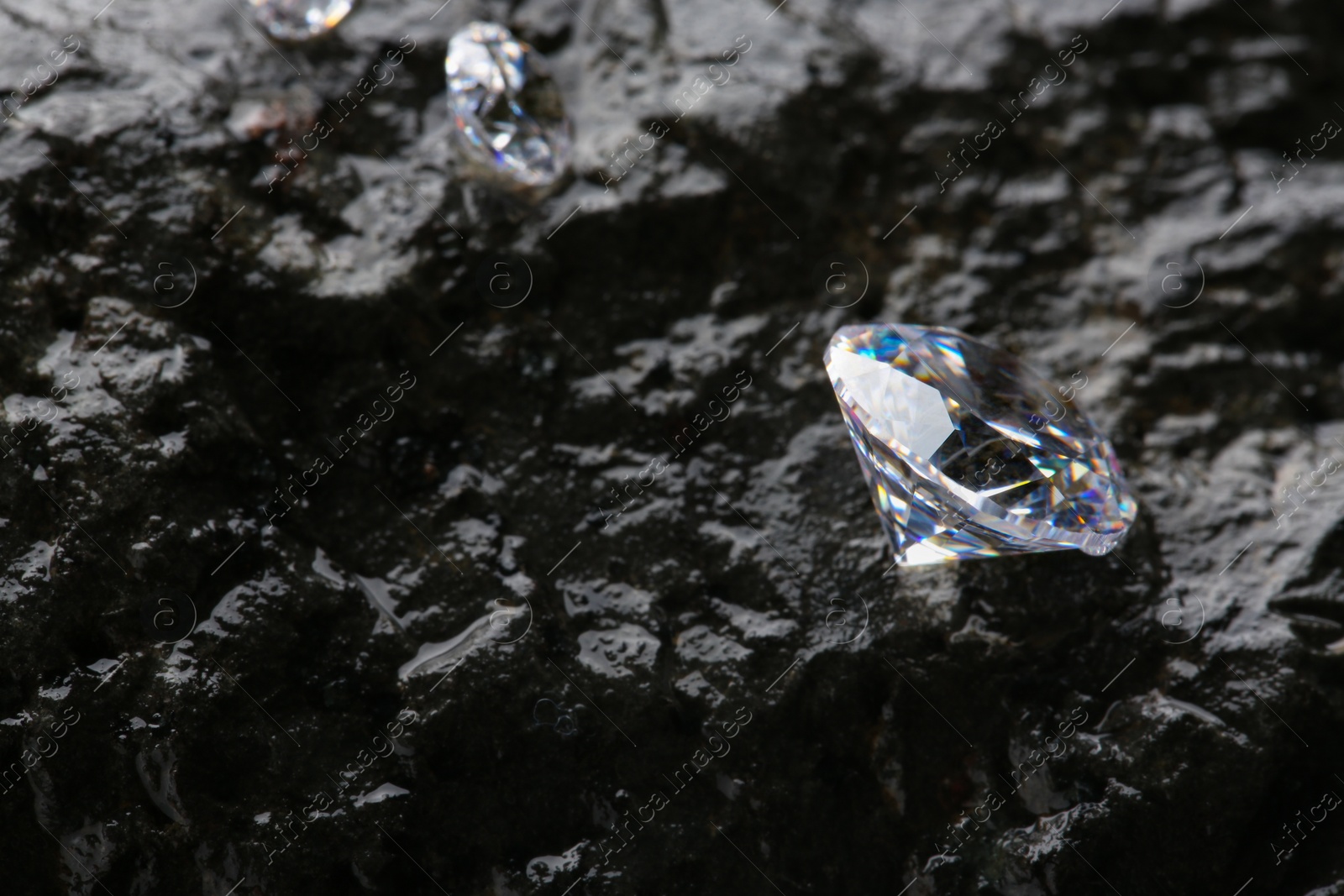 Photo of Different shiny diamonds on wet stone surface. Space for text