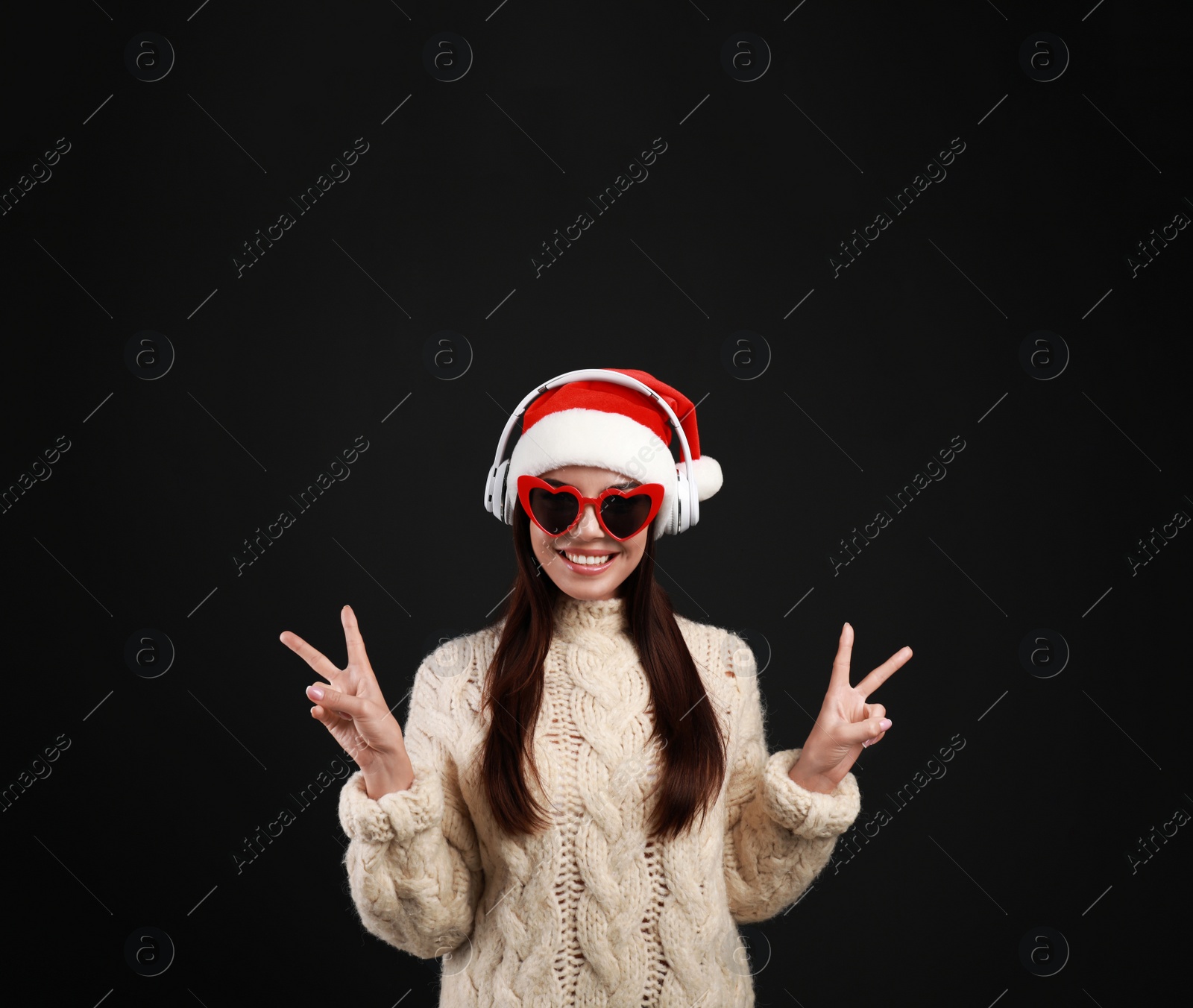 Photo of Young woman in Santa hat listening to Christmas music on black background