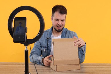 Photo of Happy fashion blogger with parcels recording video at table against orange background