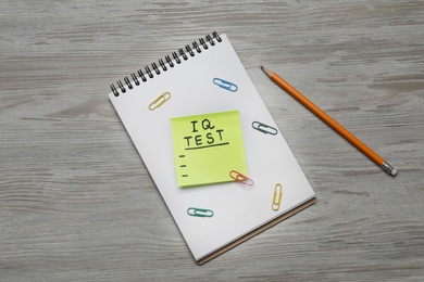 Photo of Sticky paper with words IQ Test, notebook and pencil on wooden table, flat lay