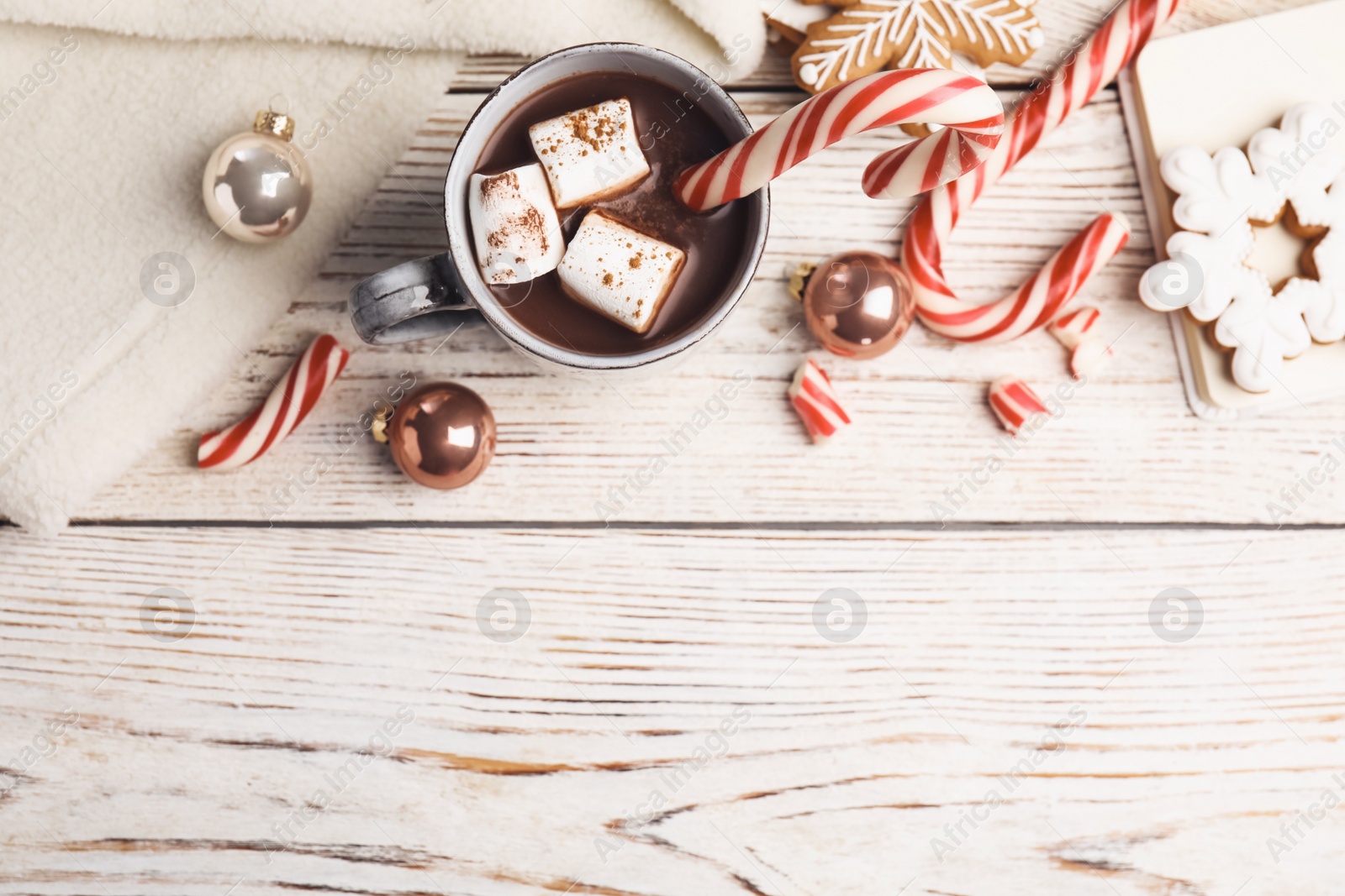 Photo of Flat lay composition with cup of tasty cocoa and Christmas candy canes on white wooden table, flat lay. Space for text