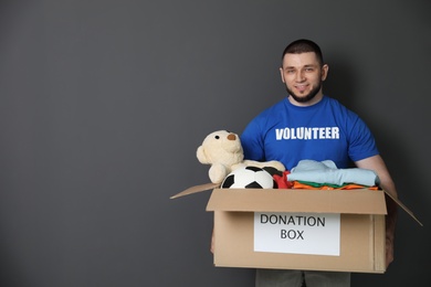 Photo of Male volunteer holding box with donations on grey background. Space for text
