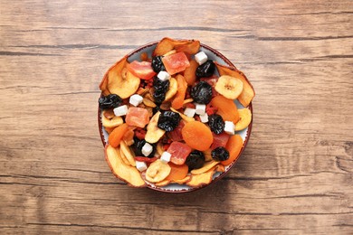 Photo of Bowl with different tasty dried fruits on wooden table, top view