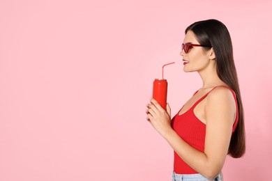 Photo of Beautiful young woman with stylish sunglasses drinking from tin can on pink background. Space for text