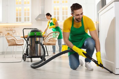 Photo of Professional janitor in uniform vacuuming floor indoors